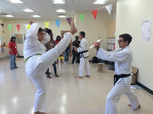 Wendy demonstrates a nice high axe kick to break the board Cei is holding.